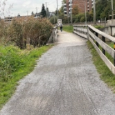 Ein Kiesweg mit grüner Wiese zu beiden Seiten und ein Holzgeländer rechts.