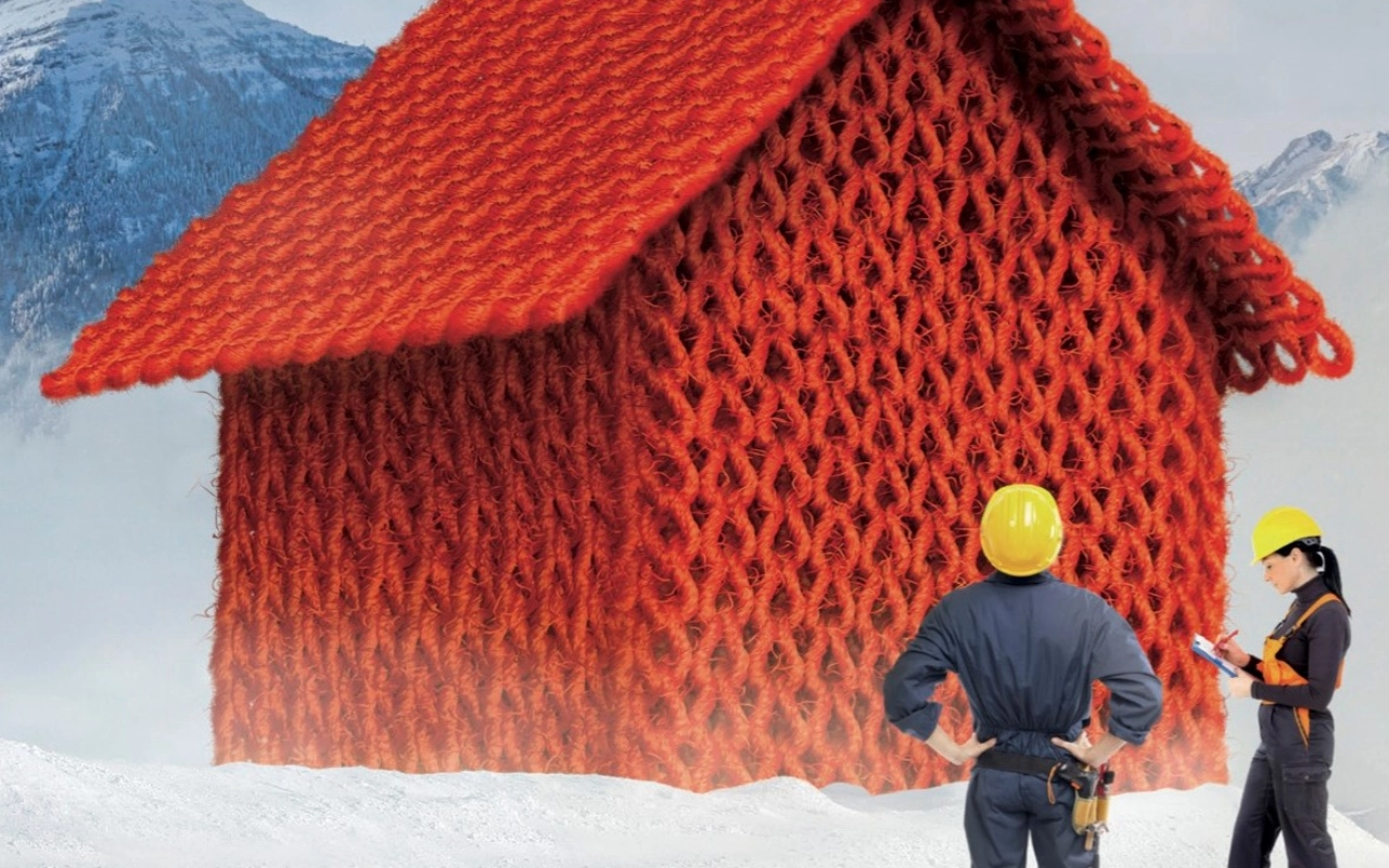 Ein rotes, gestricktes Haus in einer Schneelandschaft wird von einer Ingenieurin und einem Ingenieur auf die Wärmedämmung geprüft.